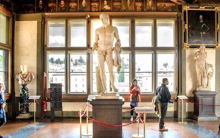 Statues and visitors inside the Uffizi Gallery, Florence, during a guided tour.