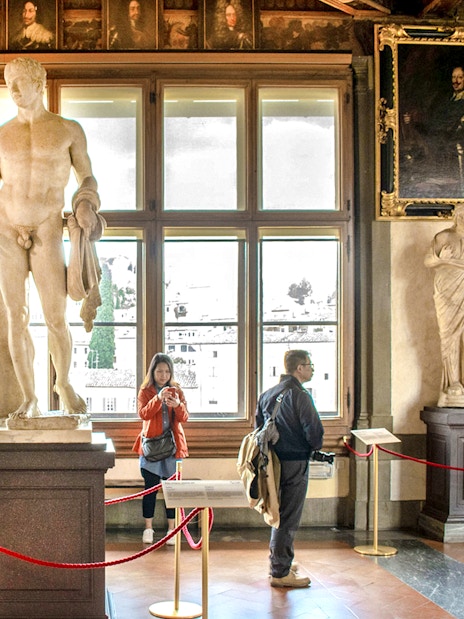 Statues and visitors inside the Uffizi Gallery, Florence, during a guided tour.