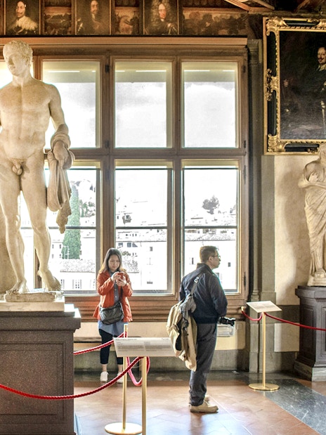 Statues and visitors inside the Uffizi Gallery, Florence, during a guided tour.