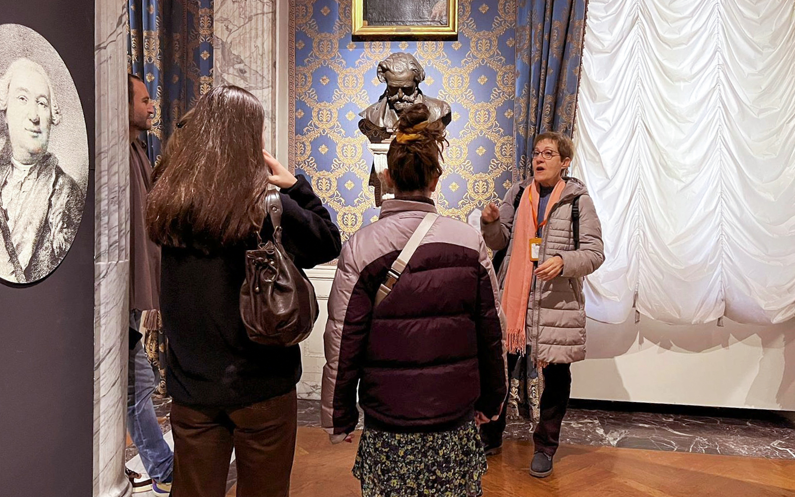 Guide explaining to tourists inside La Scala Theatre with a bust in the background.