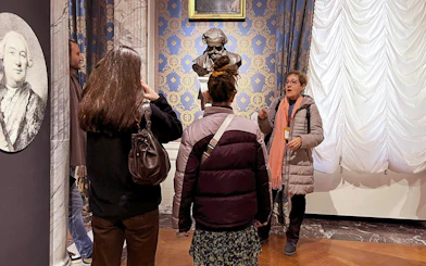 Guide explaining to tourists inside La Scala Theatre with a bust in the background.