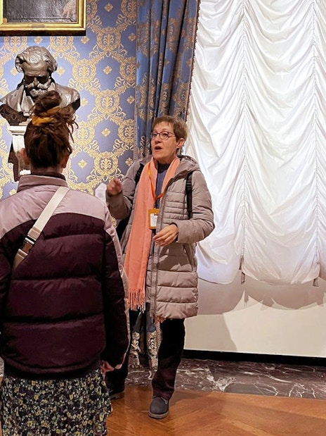 Guide explaining to tourists inside La Scala Theatre with a bust in the background.