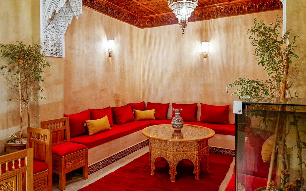 Traditional Moroccan hammam lounge with red cushions and ornate wooden table.
