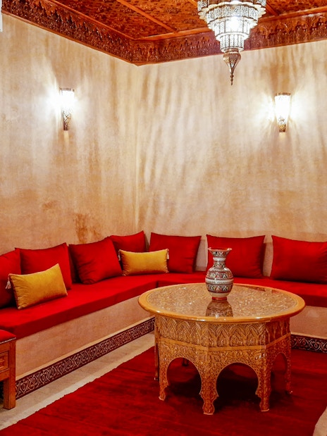 Traditional Moroccan hammam lounge with red cushions and ornate wooden table.