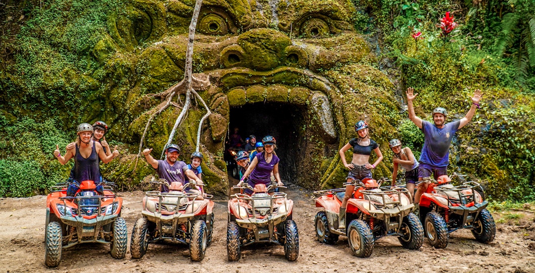 ATV riders in front of a carved stone face in Ubud's jungle setting.