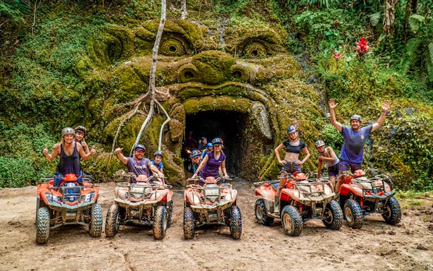 ATV riders in front of a carved stone face in Ubud's jungle setting.