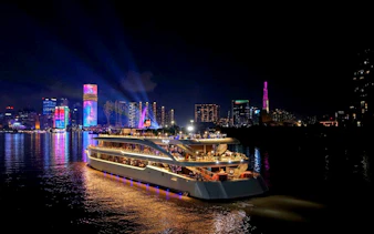 Dinner cruise on Saigon River with illuminated Ho Chi Minh City skyline at night.