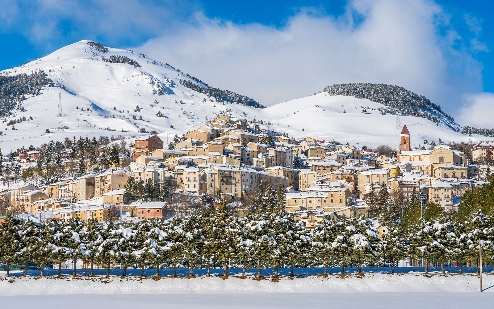 Skiers on snowy slopes in Roccaraso, Italy, with pine trees and mountains in the background.