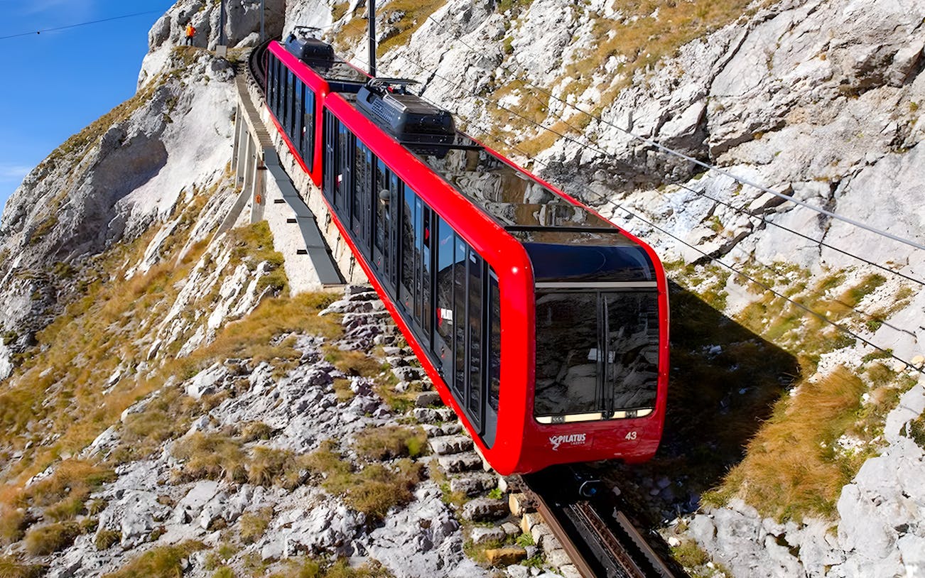 Rack railroad train ascending Pilatus Kulm from Alpnachstad through rocky terrain.