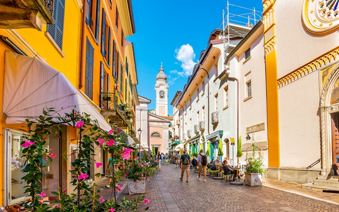 Colorful buildings and cobblestone street in Como, Italy, with people dining outdoors.