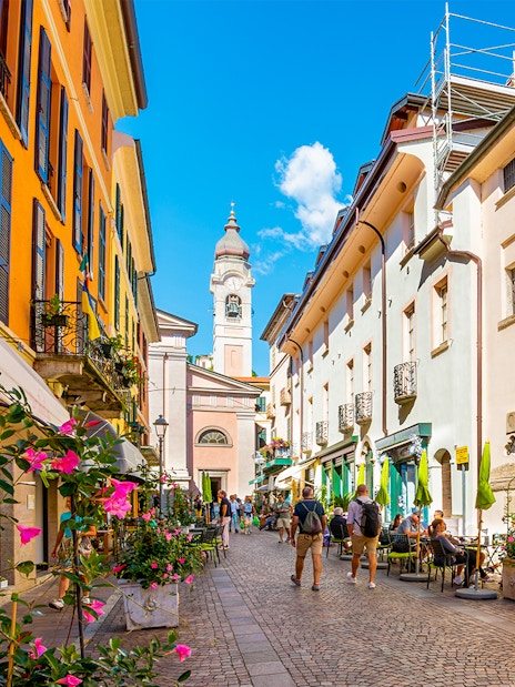 Colorful buildings and cobblestone street in Como, Italy, with people dining outdoors.