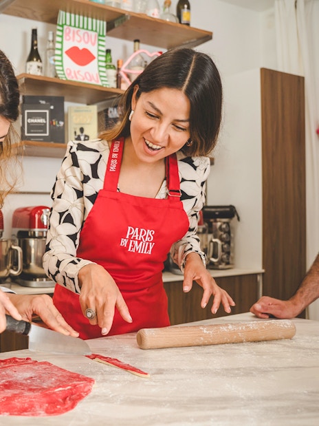 People making croissants at Emily in Paris workshop, using red dough and kitchen tools.