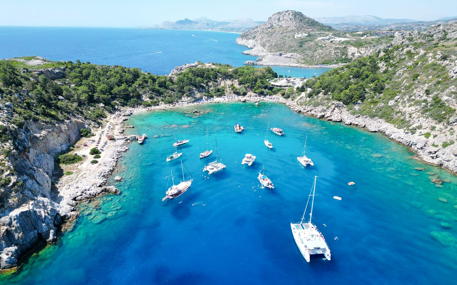 Sailboats anchored in Anthony Quinn Bay, Rhodes, surrounded by rocky cliffs and clear blue water.