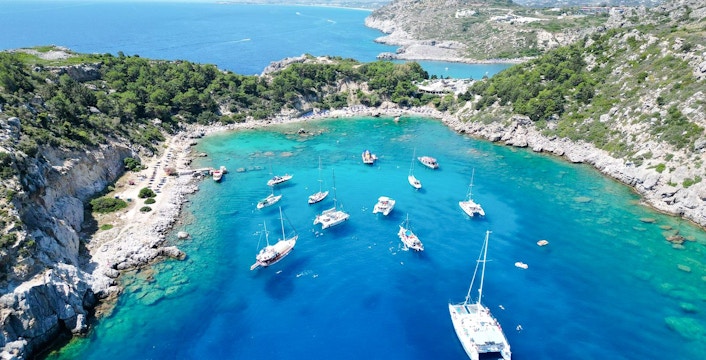 Sailboats anchored in Anthony Quinn Bay, Rhodes, surrounded by rocky cliffs and clear blue water.
