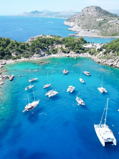 Sailboats anchored in Anthony Quinn Bay, Rhodes, surrounded by rocky cliffs and clear blue water.