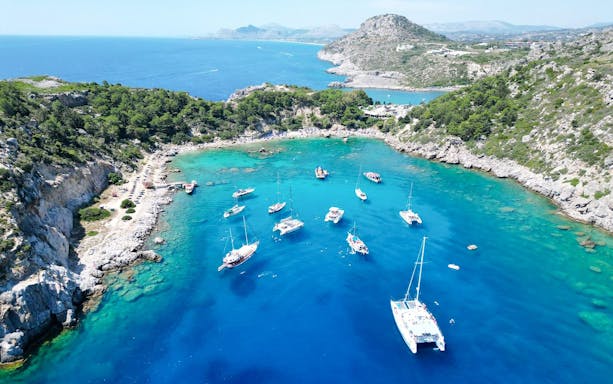Sailboats anchored in Anthony Quinn Bay, Rhodes, surrounded by rocky cliffs and clear blue water.
