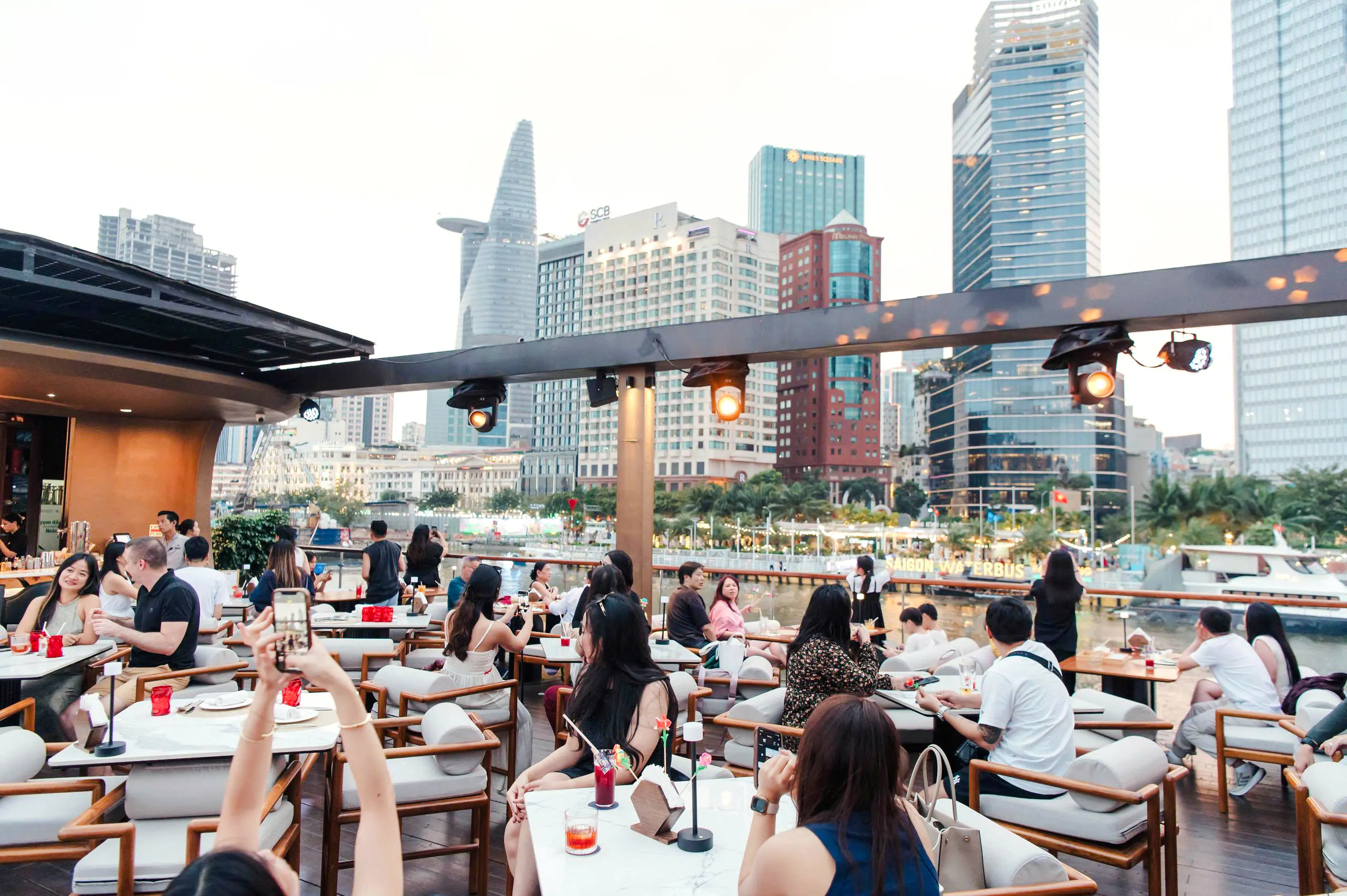 People dining on a river cruise with Ho Chi Minh City skyline in the background.