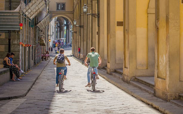 Cyclists on e-bike tour through narrow street in Florence, Italy.