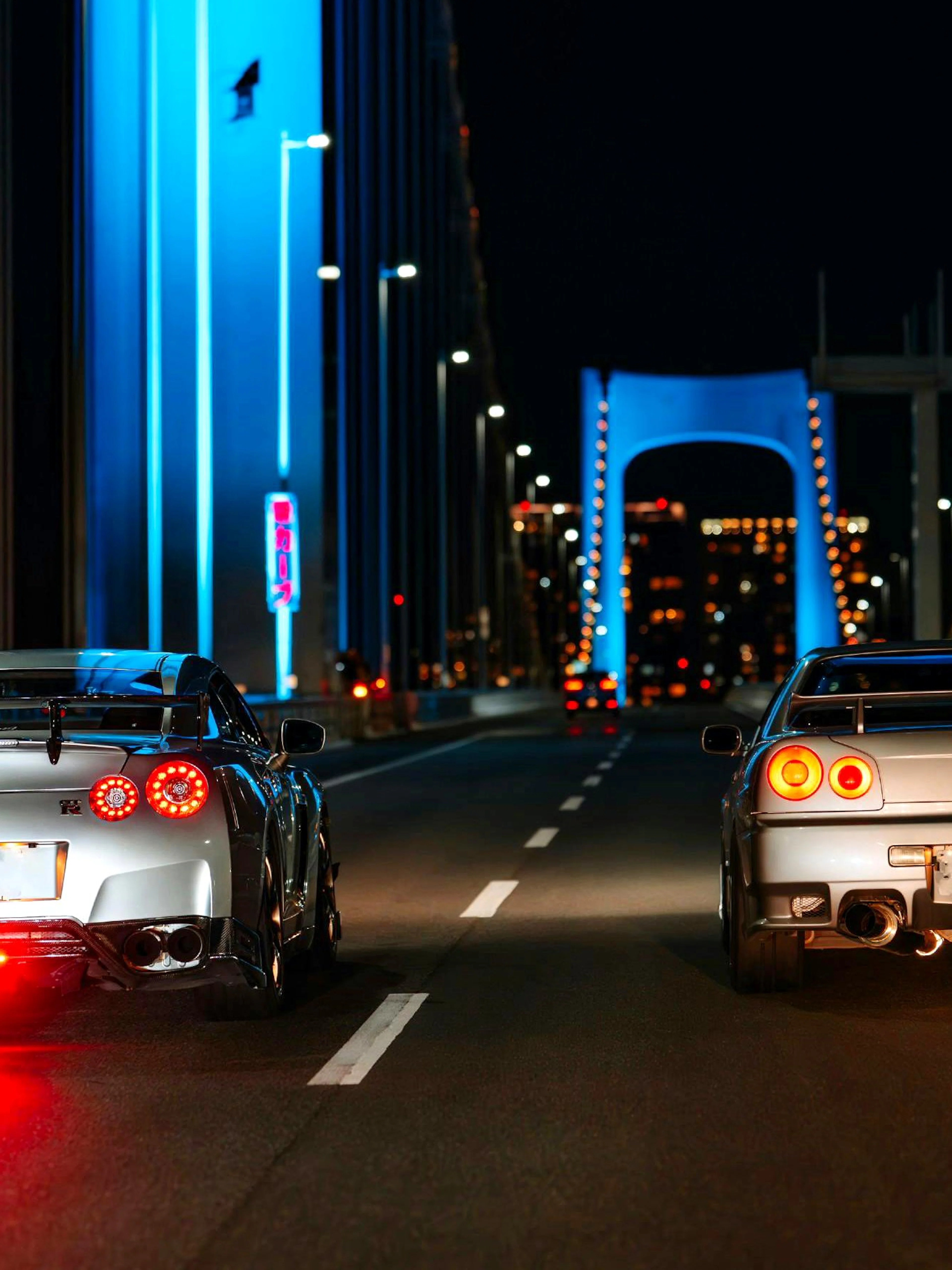 Two sports cars on a Tokyo bridge at night during JDM car meetup tour.