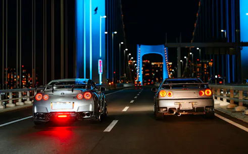 Two sports cars on a Tokyo bridge at night during JDM car meetup tour.