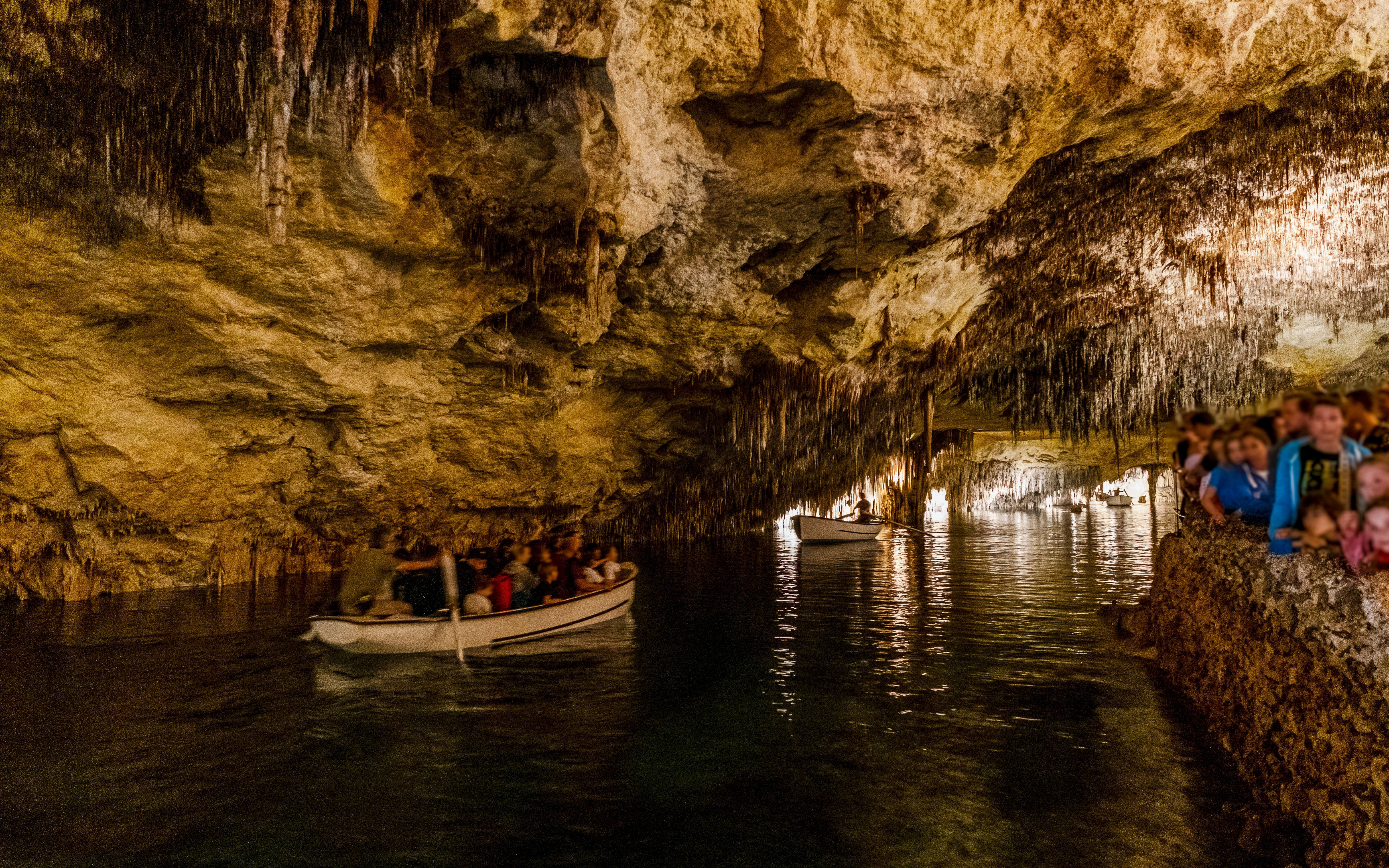 Boat tour inside Drach Caves, Mallorca, Spain with people exploring the illuminated cavern.