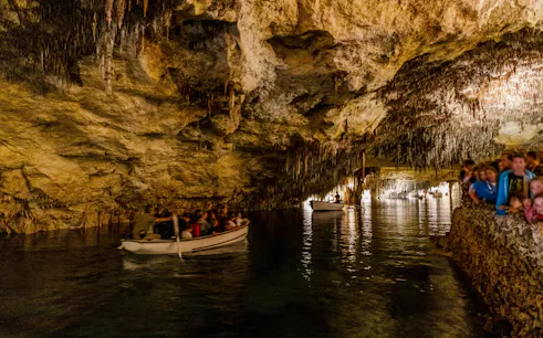 Boat tour inside Drach Caves, Mallorca, Spain with people exploring the illuminated cavern.