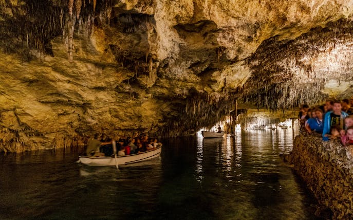 Boat tour inside Drach Caves, Mallorca, Spain with people exploring the illuminated cavern.