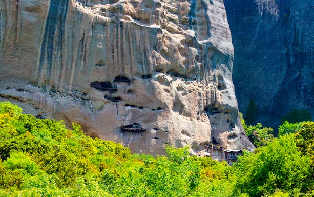 Hermit caves carved into the cliffs at Meteora, Greece, surrounded by lush greenery.