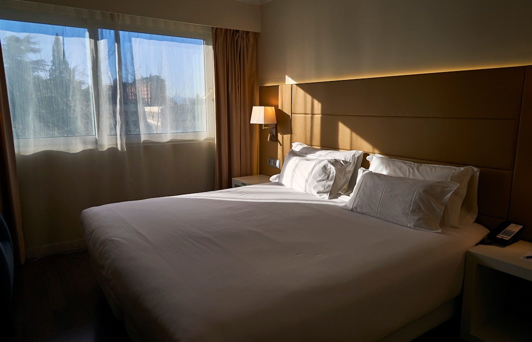 Modern hotel room with a large bed, desk, and window view in a city location.