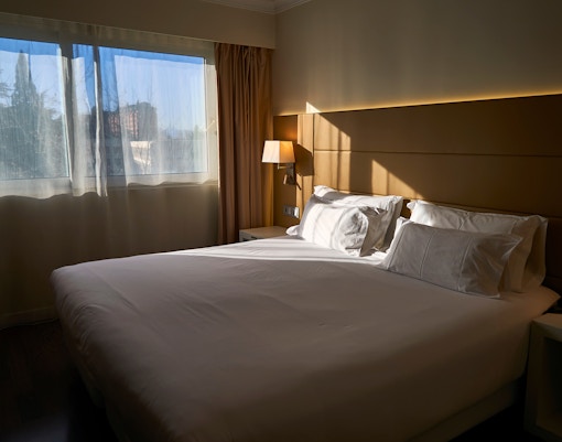 Modern hotel room with a large bed, desk, and window view in a city location.