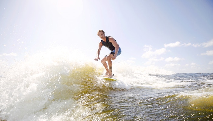 Man wakeboarding on waves in Dubai under a clear sky.