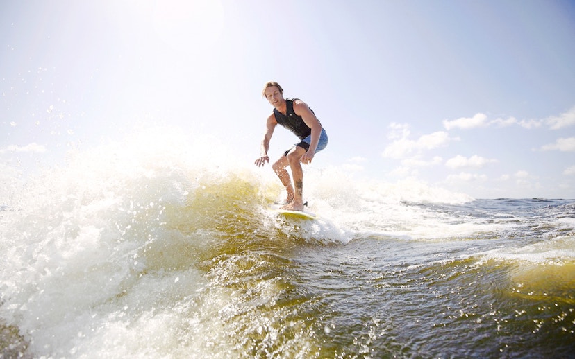 Man wakeboarding on waves in Dubai under a clear sky.