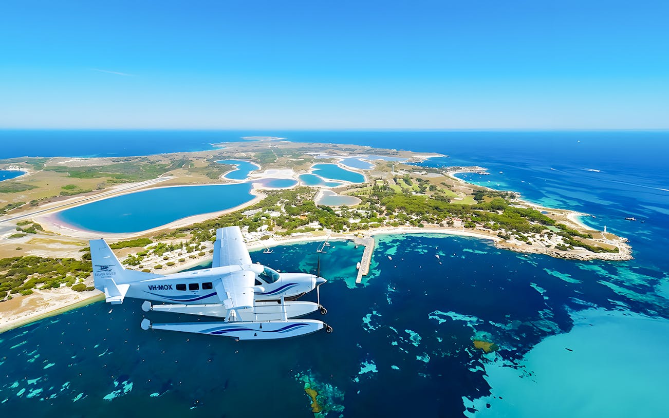 Aerial view of Rottnest Island with a seaplane flying over turquoise waters.