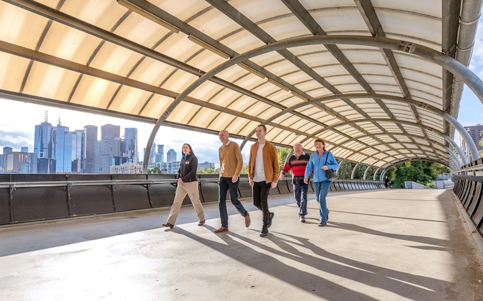 Group walking on a covered bridge with Melbourne skyline in the background.
