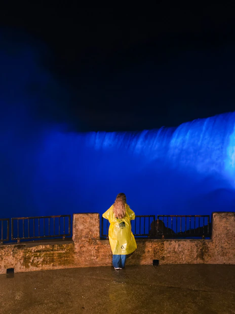 Person in yellow raincoat viewing illuminated Niagara Falls at night.