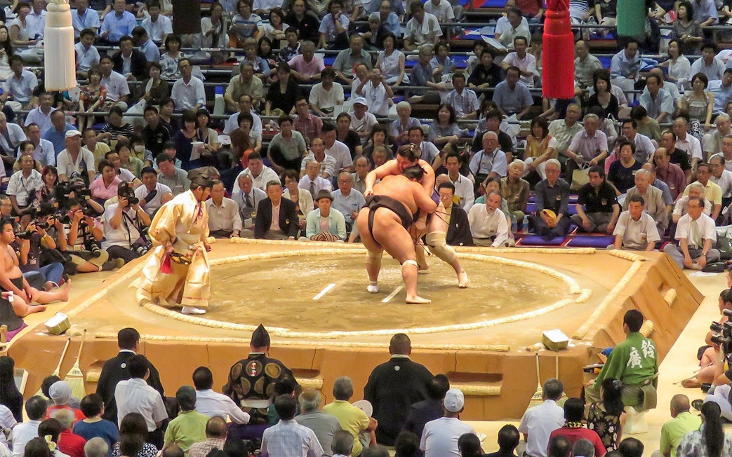 Sumo wrestlers competing in a Fukuoka tournament with a large audience watching.