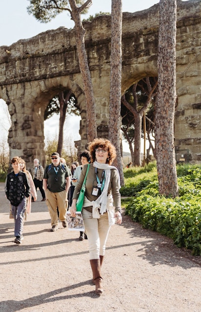 Tour group walking by ancient Roman aqueducts on the Appian Way in Rome.