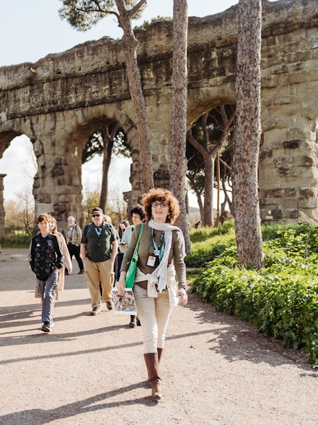 Tour group walking by ancient Roman aqueducts on the Appian Way in Rome.