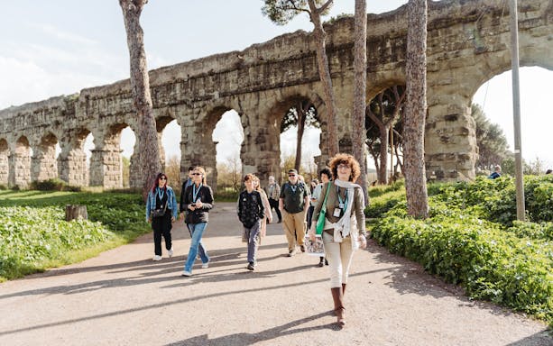 Tour group walking by ancient Roman aqueducts on the Appian Way in Rome.