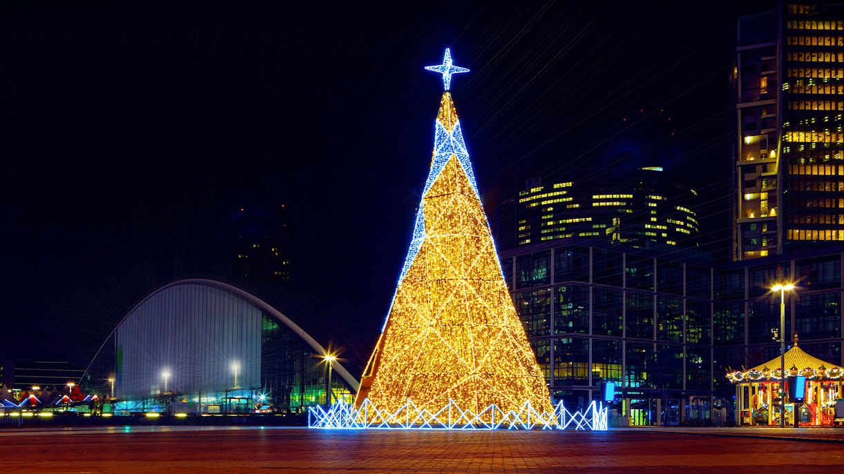 Christmas tree illuminated with lights at night in Paris, with city buildings in the background.