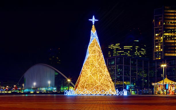 Christmas tree illuminated with lights at night in Paris, with city buildings in the background.