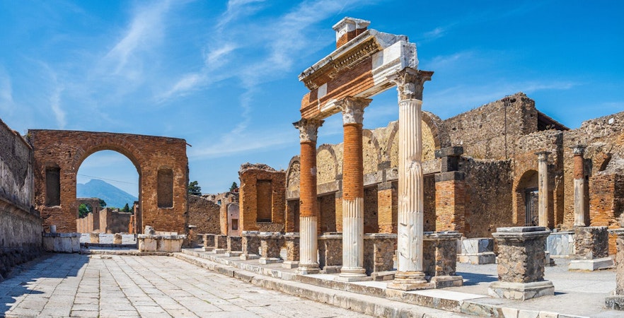 Ancient ruins of Pompeii with stone columns and archway under a clear blue sky.