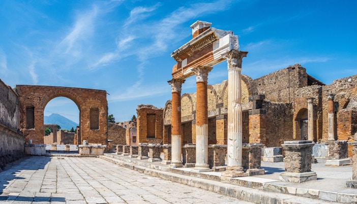 Ancient ruins of Pompeii with stone columns and archway under a clear blue sky.