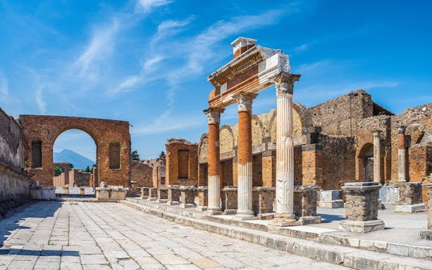 Ancient ruins of Pompeii with stone columns and archway under a clear blue sky.