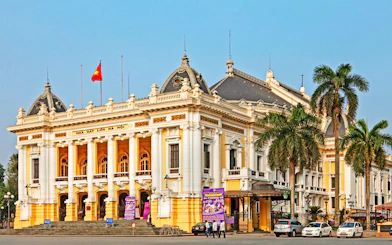 Hanoi Opera House with palm trees and cars in front, part of the Hanoi city highlights tour.