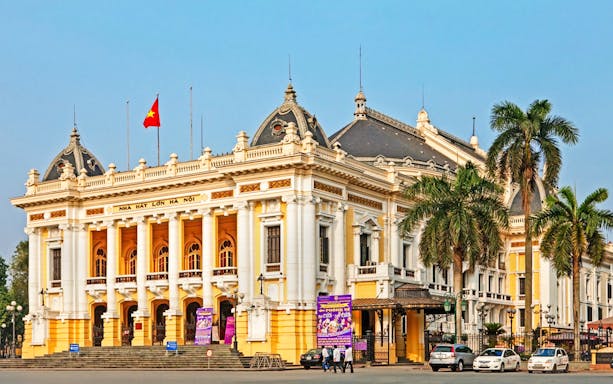 Hanoi Opera House with palm trees and cars in front, part of the Hanoi city highlights tour.