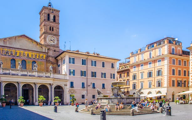 People strolling in Piazza di Santa Maria, Trastevere, Rome, near the basilica and fountain.