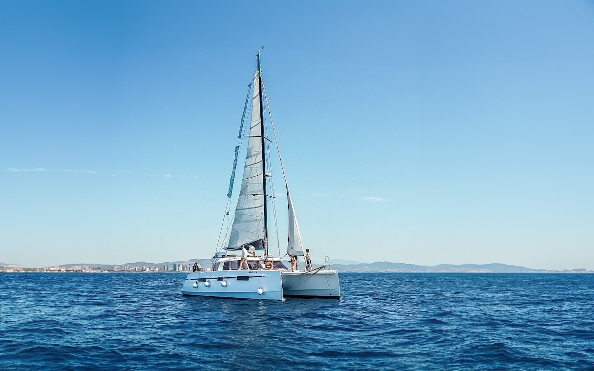 Eco-catamaran sailing near Barcelona coastline.