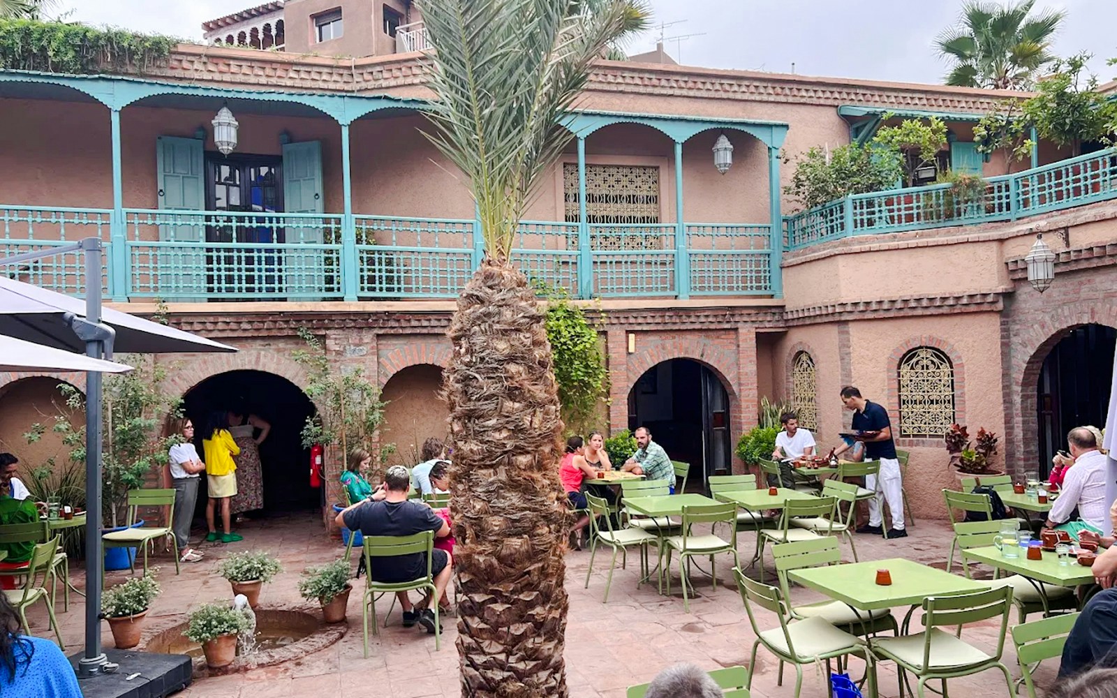 Jardin Majorelle cafe courtyard with visitors seated at green tables, Marrakech.