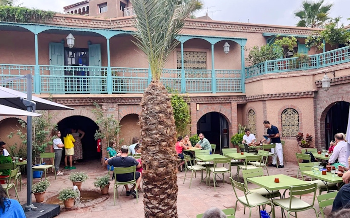 Jardin Majorelle cafe courtyard with visitors seated at green tables, Marrakech.